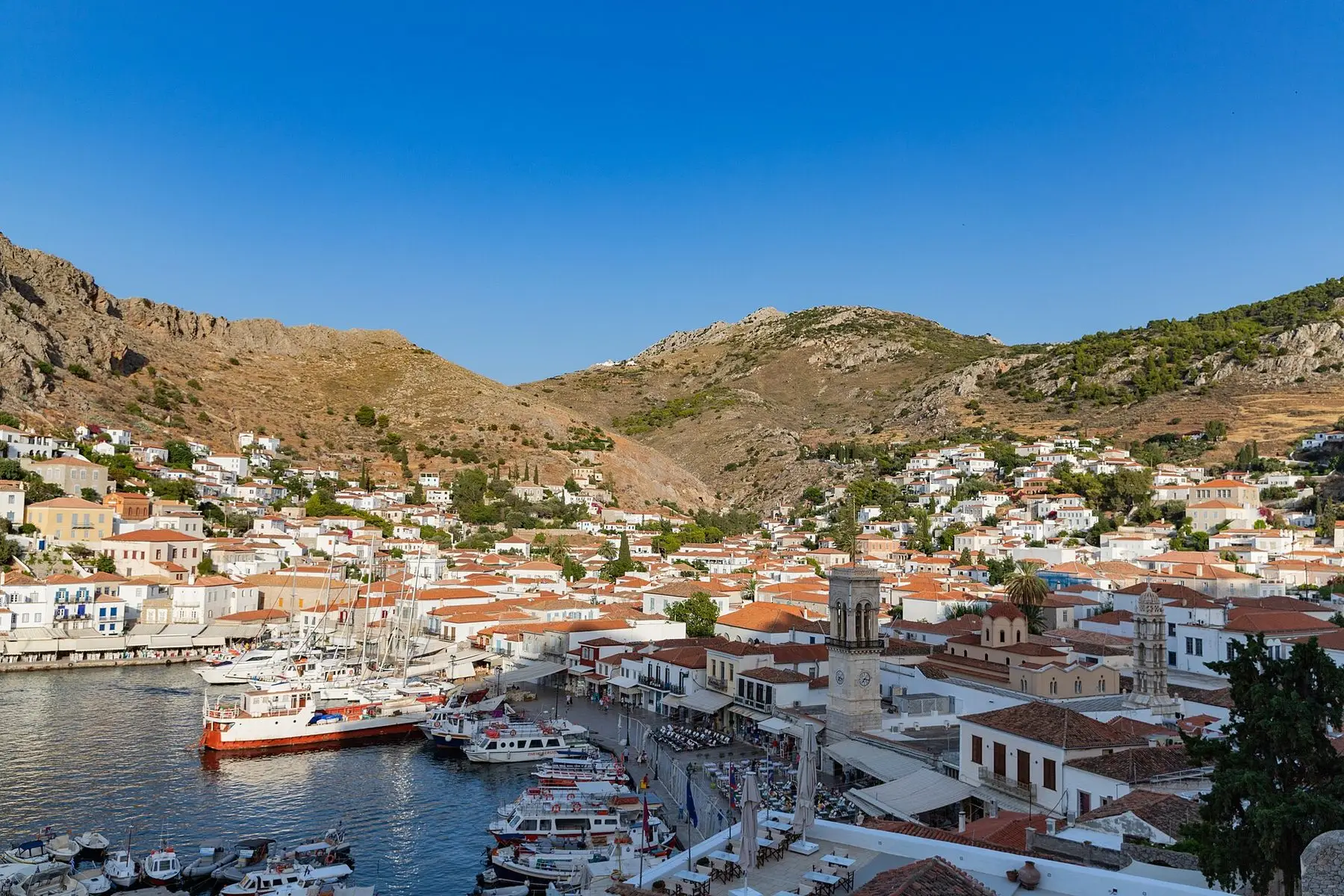 Puerto de piedra del pueblo de Hidra con barcos de pesca y casas en la ladera, sin coches a la vista