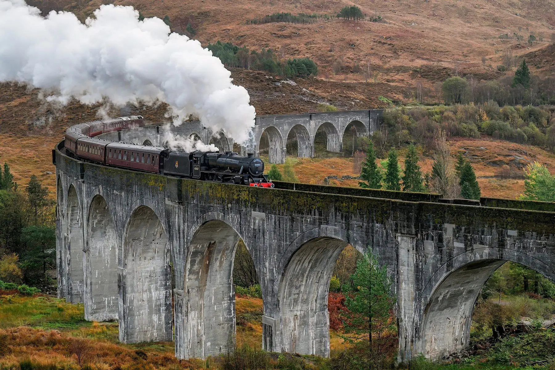 Un treno rosso della West Highland Line che attraversa il viadotto di Glenfinnan con le montagne sullo sfondo